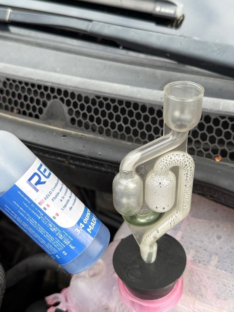 Combustion leak tester fitted to a coolant tank, with a bottle of blue test fluid beside it